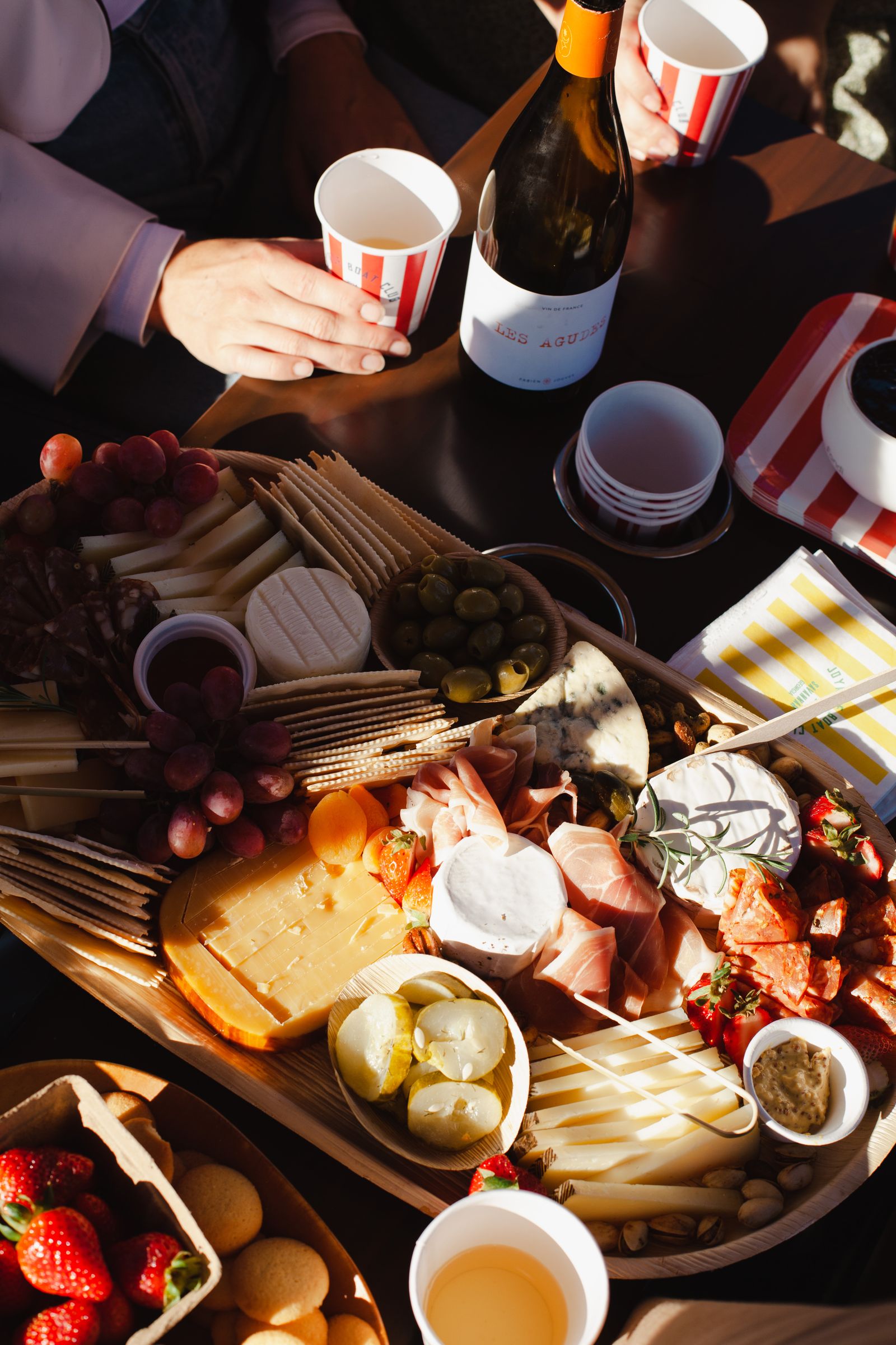 Overhead view of a Provisions Savannah charcuterie board with natural wine and red-striped Joyride cups on board